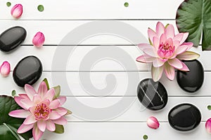 Pink lotus flowers and smooth black pebbles on a white wooden surface. Top view with copy-space