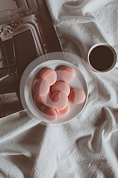 Pink macaron cookies with cup of coffee and rose flowers on white background.