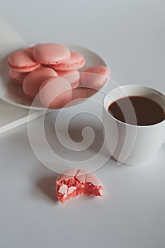 Pink macaron cookies with cup of coffee and rose flowers on white background.