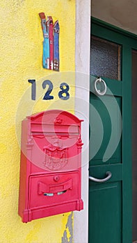 Pink mailbox on a yellow wall, next to a green door, on the island of Burano, Italy