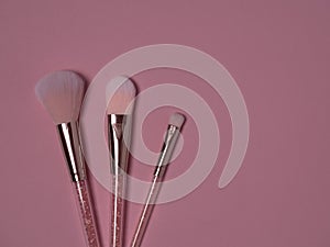 Pink makeup brushes on a pink background top view with copy space.