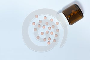 Pink medical pills and tablets spilling out of a drug bottle on the white background, top view with copy space for text, health