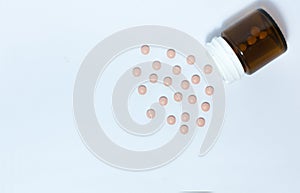 Pink medical pills and tablets spilling out of a drug bottle on the white background, top view with copy space for text, health