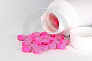 Pink medicine tablet antibiotic pills spilling out of a bottle, jar on white background