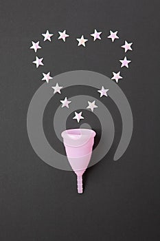 Pink menstrual cup on black background with heart, copy spase. Concept possibility of comfort use of cup at night, zero waste,