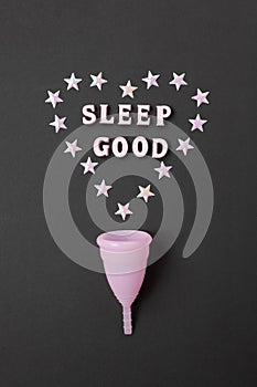 Pink menstrual cup on black background with with heart and words Sleep good. Concept possibility of use cup at night, zero waste,