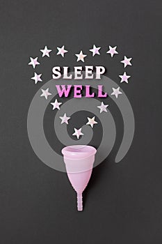 Pink menstrual cup on black background with with heart and words Sleep Well. Concept possibility of use cup at night, zero waste,