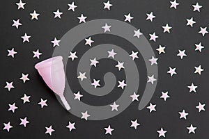 Pink menstrual cup on black background with numerous stars. Concept possibility of use cup at night, zero waste, savings,