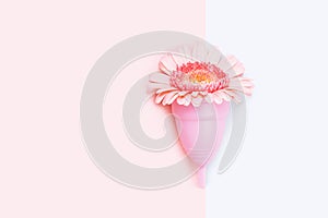 Pink menstrual cup and a flower on on pink and white background