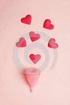 pink menstrual cup and red hearts as blood drops isolated on rose background, menstruation cycle, women gynecological health and