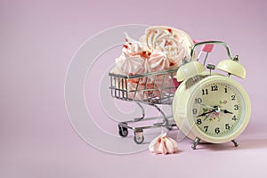 Pink mezies in a small shopping cart and an alarm clock on a pink background. Creative concept food health diet.