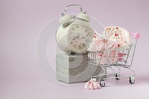 Pink mezies in a small shopping cart and an alarm clock on a pink background. Creative concept food health diet.