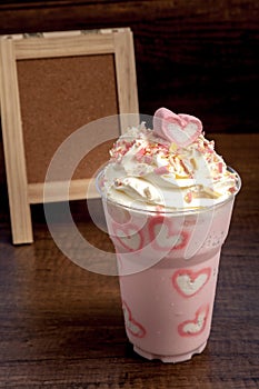 Pink milk shake with heart shape marshmellows topping on wooden