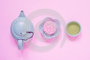 Pink mooncake, blue teapot, cup of green tea on a pink background. Chinese mid-autumn festival food