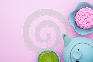 Pink mooncake, blue teapot, cup of green tea on a pink background. Chinese mid-autumn festival food