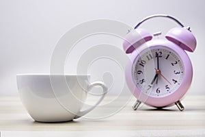 Pink mug and clock on wooden table over white background.Concept coffee break or tea time.