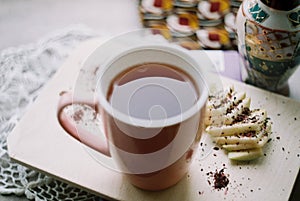 Pink mug with tea on a wooden board and a lace napkin