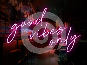 A pink neon style Good Vibes Only sign in front of a bar or pub. Slightly blurred bar or tavern background.