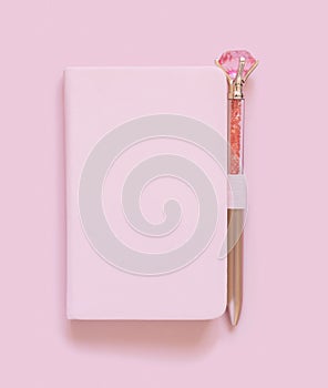 Pink notebook and deorative gemstone pen on light pink top view