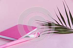 Pink notebook for notes, funny flamingo pen and green palm leaves on pink pastel background
