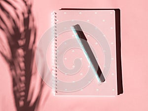 Pink notebook with pen and tropical plant shadow