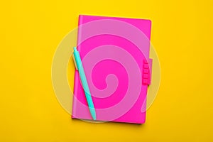 Pink notebook and pen on yellow background, top view