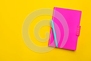 Pink notebook and pen on yellow background. Space for text