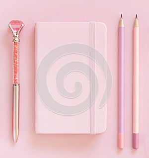 Pink notebook, pensils and decorative gemstone pen on light pink top view