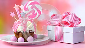 Pink novelty cupcake decorated with candy and large lollipop.