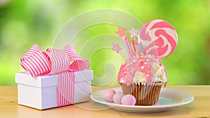 Pink novelty cupcake decorated with candy and lollipop against garden background