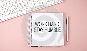 Pink office desk with keyboard and notebook with text WORK HARD STAY HUMBLE