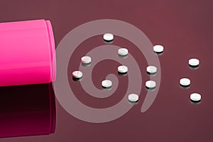 Pink open bottle and pills.Tablets spilling from container