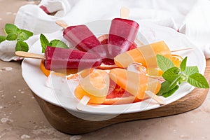 Pink and orange popsicle with red oranges on grey stone background.