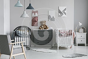 Pink organizer on wall of trendy baby bedroom with two cribs and chest of drawers