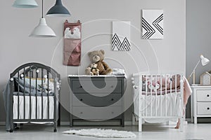 Organizer on wall of trendy baby bedroom with two cribs and chest of drawers