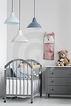 Pink organizer on wall of trendy baby bedroom with two cribs and chest of drawers