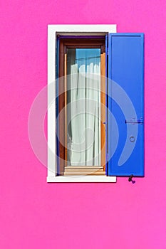 Pink painted facade of the house and window with blue shutters. Burano, Venice, Italy