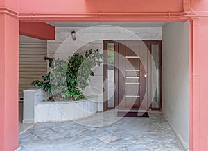 Pink painted portico of an apartment building entrance covered with white marble, potted plants and a dark wood door.