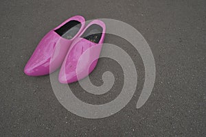 Pink painted wooden shoes on the gray asphalt