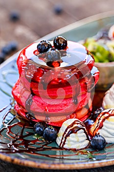 Pink pancakes with honey, chocolate, jam, whipped cream, berries and fruits on plate.