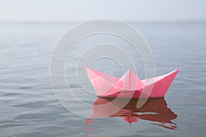 Pink paper boat on water surface, space for text