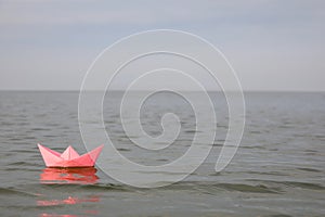 Pink paper boat on water surface, space for text