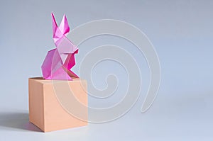 Pink paper hare on an orange cube on a light background.
