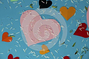 pink paper heart on a blue background, around many colorful hearts covered with daisy flower petals,