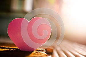 Pink paper heart shape on wooden with over light day.