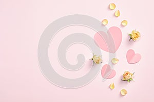 Pink paper hearts and yellow rose buds flowers and petals on pastel pink background. Valentines day flat lay style composition,