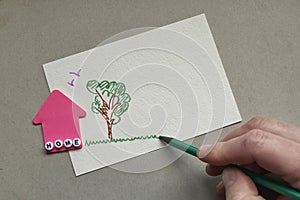 Pink paper house with word Home made of letters and male hand draws tree and grass. Stay at Home picture. Coronavirus