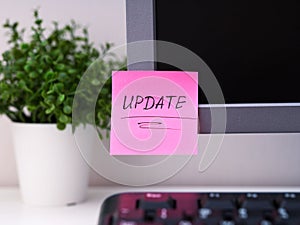 A pink paper notes with the reminder Update on it sticked on to a monitor at an office workplace