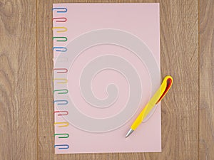 Pink paper sheet fixed with multi-colored paper clips on oak Board table close, yellow ballpoint pen