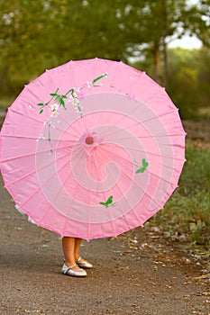 Pink parasol with little girl's legs and feet showing from behind